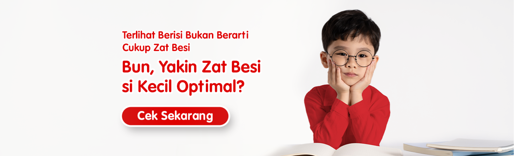 Anak laki-laki mengenakan baju merah dan kacamata, duduk membaca buku dengan pesan pentingnya memastikan kecukupan zat besi anak